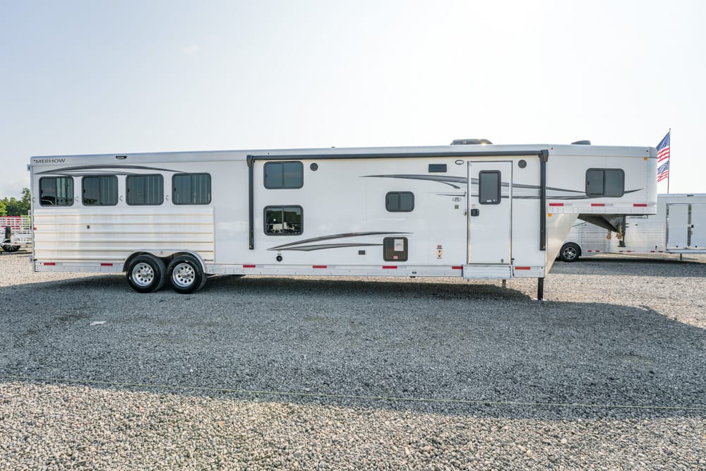 White fifth-wheel RV trailer on a gravel lot, with an American flag at the rear and extended hitch area visible
