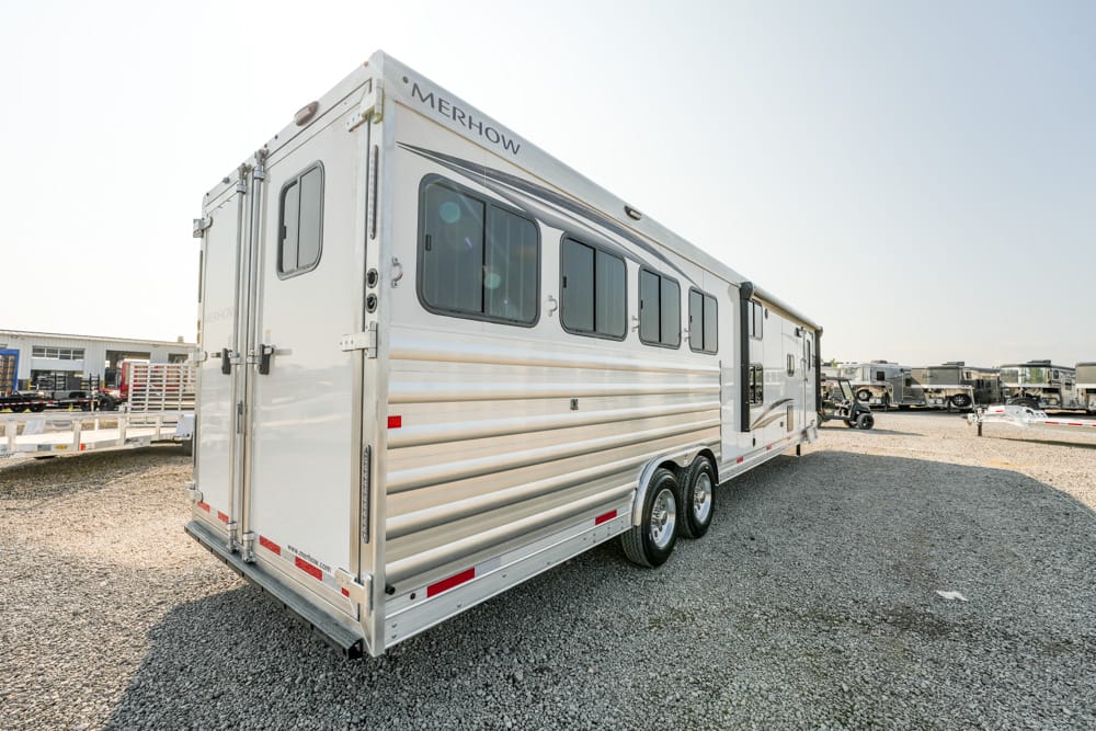 Silver Merhow horse trailer with multiple windows and dual axles parked on a gravel lot.