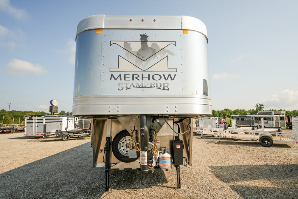 Silver Merhow Stampede horse trailer seen from the front in a trailer lot, with a spare tire, propane tank, and hitch visible beneath the elevated living quarters.