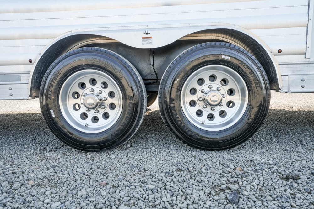 Dual trailer wheels with silver rims on a gravel surface