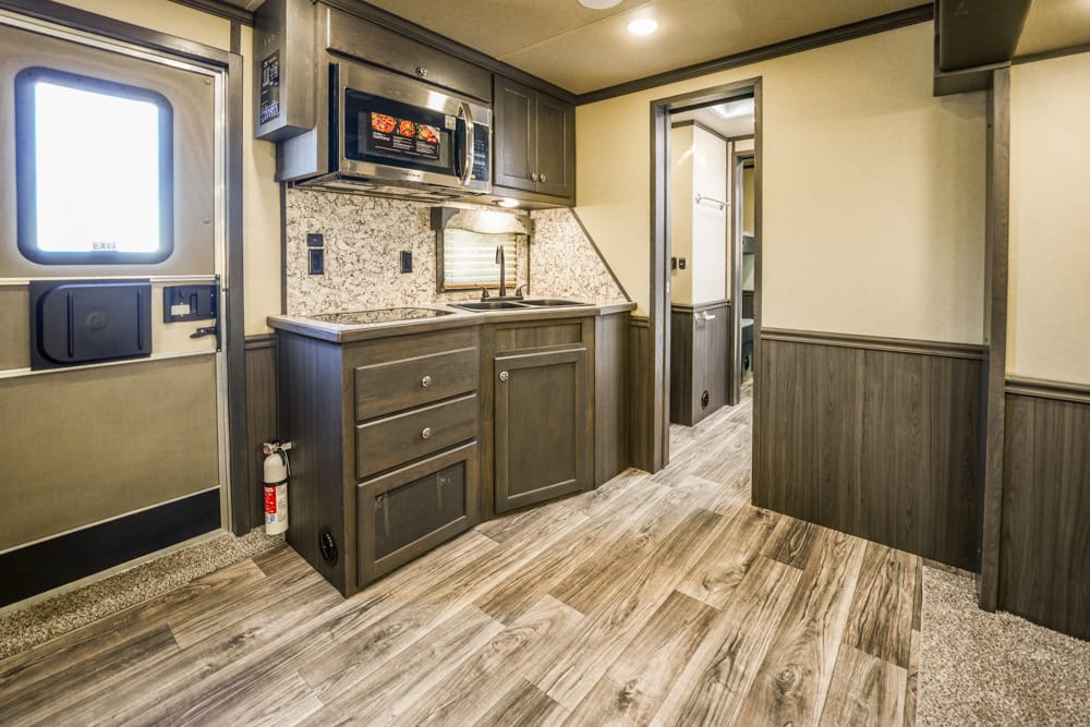 RV kitchen with dark wood cabinets, granite countertop, microwave, and a doorway leading to a hallway.