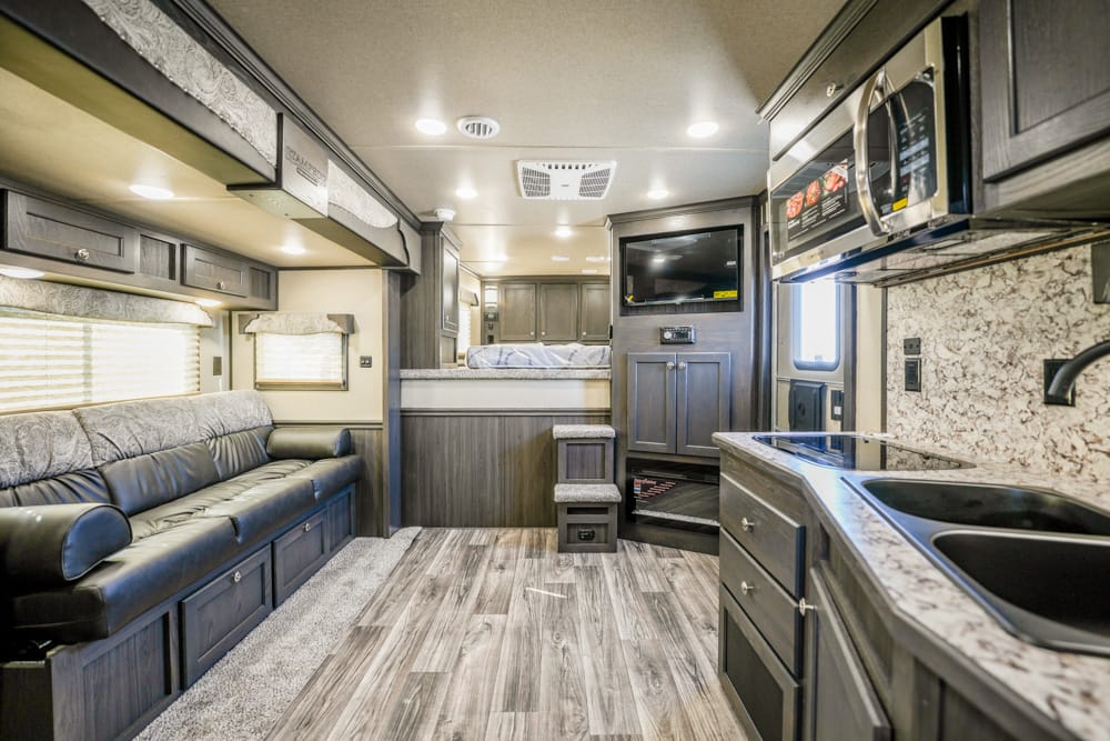 Modern RV interior showing a long leather sofa, overhead cabinets, and a wood-look floor.