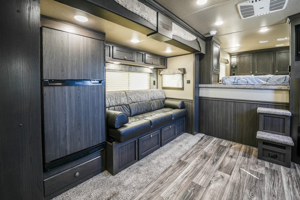Interior of a dark wood RV with a gray leather sofa and overhead cabinets, front living area layout indoors