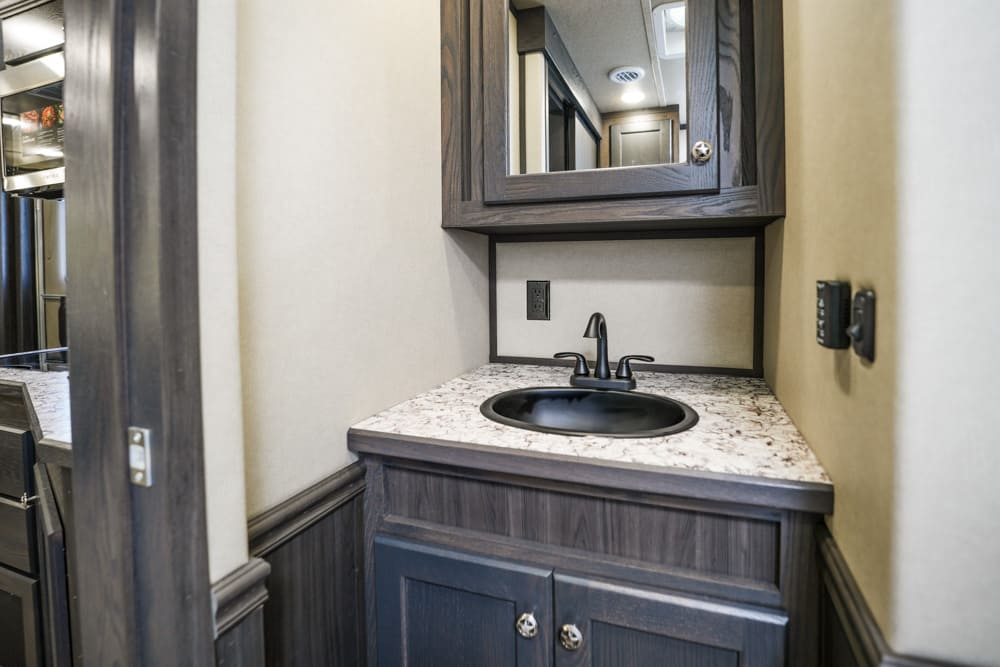 Compact bathroom vanity with dark wood cabinet, black sink, and marble countertop; mirrored cabinet above in an RV or small space.
