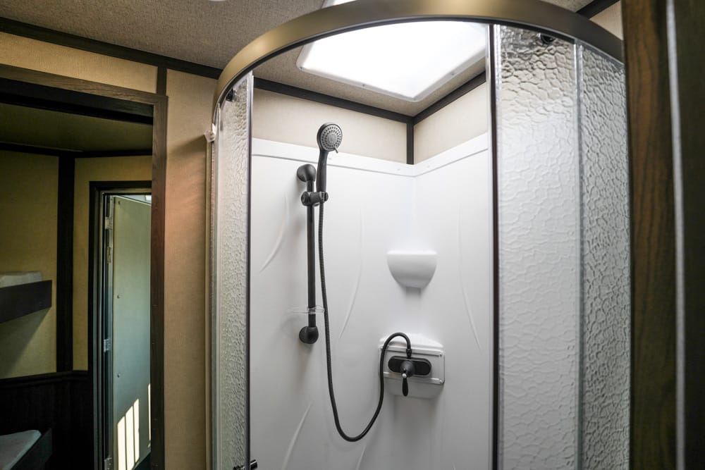 Shower stall with a handheld shower head, soap dish, and built-in controls inside a small bathroom closet-like space. Blind curve doors and frosted glass panels surround the shower.