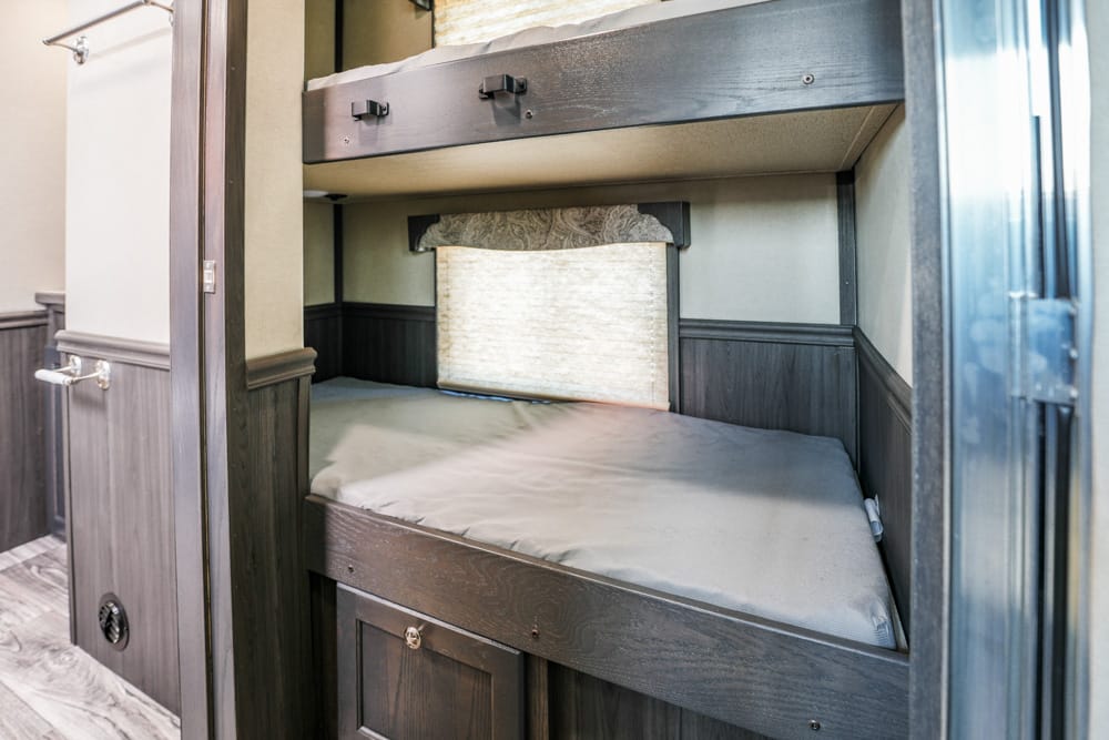 Dark wood built-in bunk beds in a small RV-style room, with a lower bunk mattress and an upper bunk above.