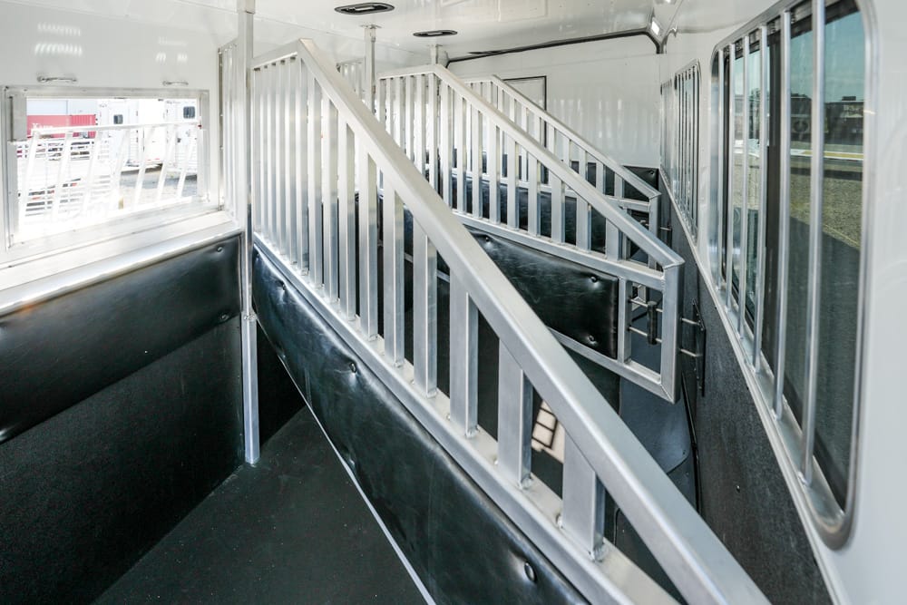 Interior of a white utility trailer with metal divider rails and a stairway leading to a raised section.