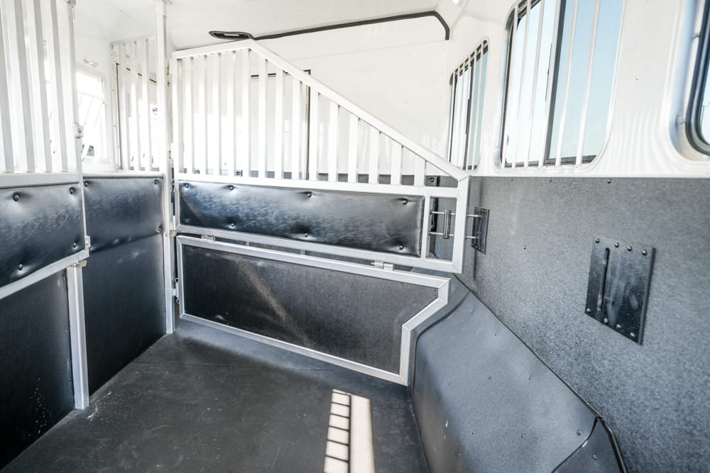Interior of an empty horse trailer with metal partition bars and padded gray walls on either side.