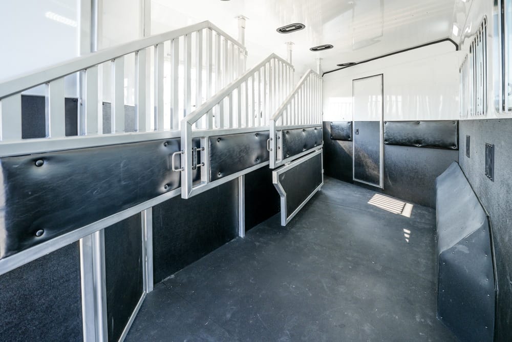 Interior of a clean horse trailer with two metal stalls and white dividing rails.