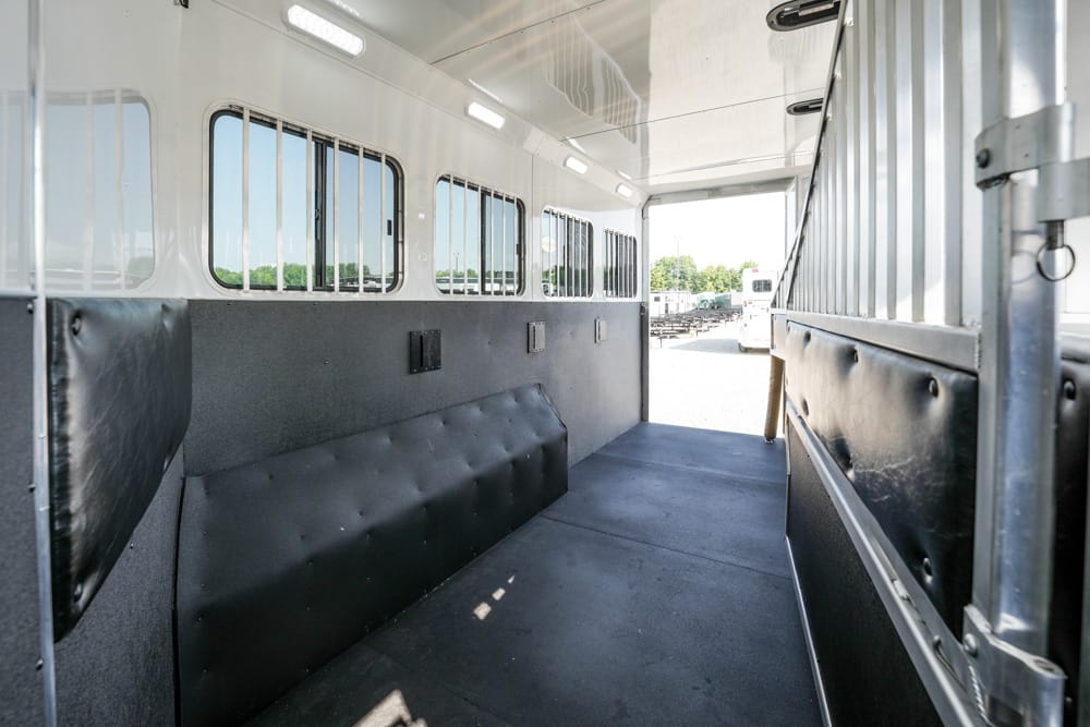 Interior of an empty livestock trailer with padded walls and side windows, looking toward the open rear door.