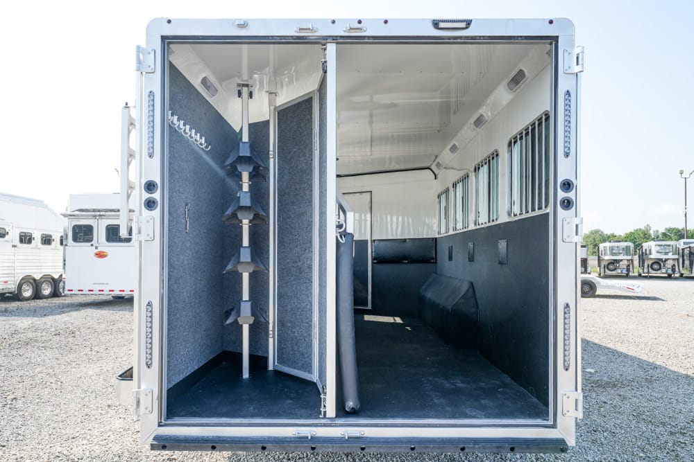 Interior of an empty horse trailer showing partition and stall dividers along blue padded walls and hooks on the left wall.
