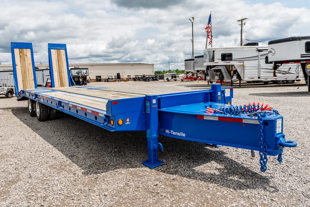 Blue Hi-Tensile flatbed semi-trailer on a gravel lot, with wooden deck and rear ramps raised up front left of the image.