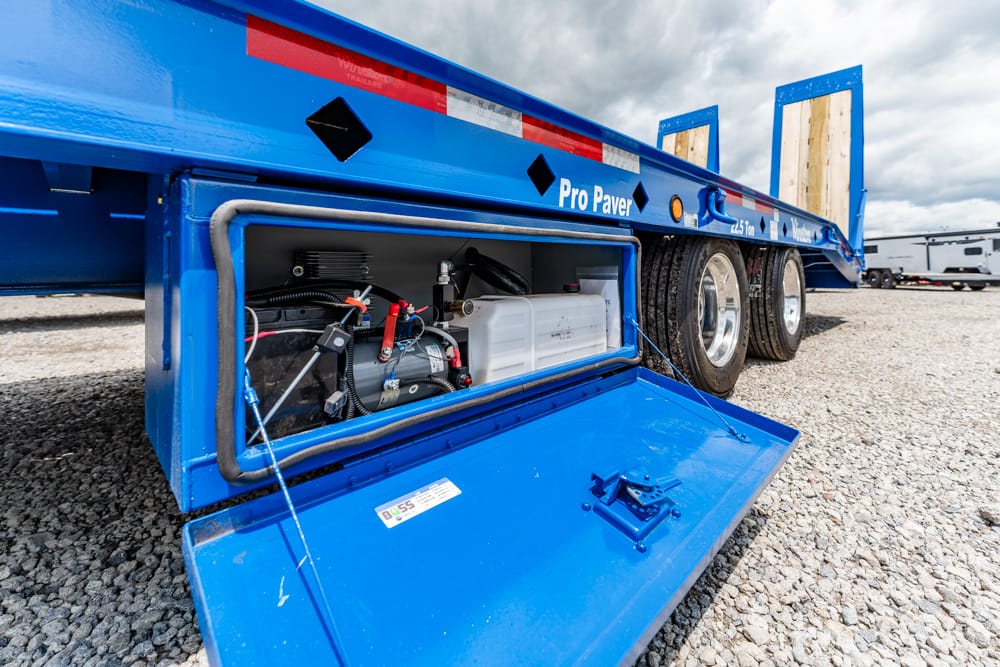 Blue flatbed trailer with its service panel open, revealing a small generator and white fuel tank inside the storage compartment.