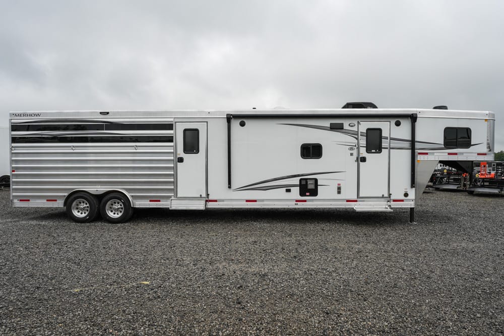 Profile view of a long white fifth-wheel trailer with silver siding and gray decorative stripes, parked on a gravel lot under a cloudy sky.