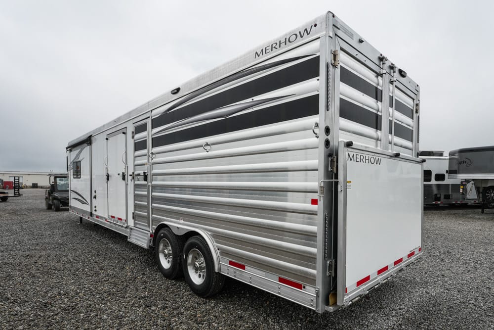Silver Merhow horse trailer with two axles and a rear ramp, parked on a gravel lot.