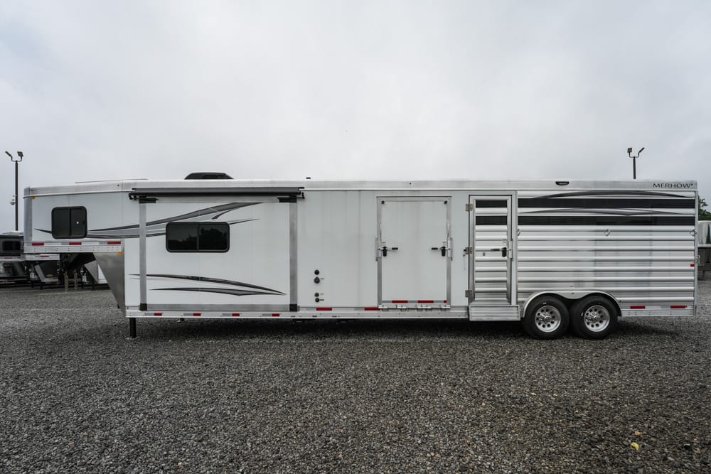 Long white horse/livestock trailer with two axles and side doors, parked on a gravel lot.