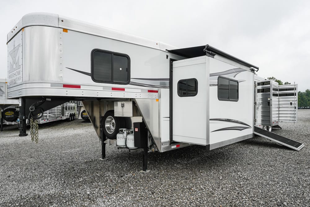 Fifth-wheel RV trailer with a raised front, slide-out room extended, and a side entry with stairs on a gravel lot