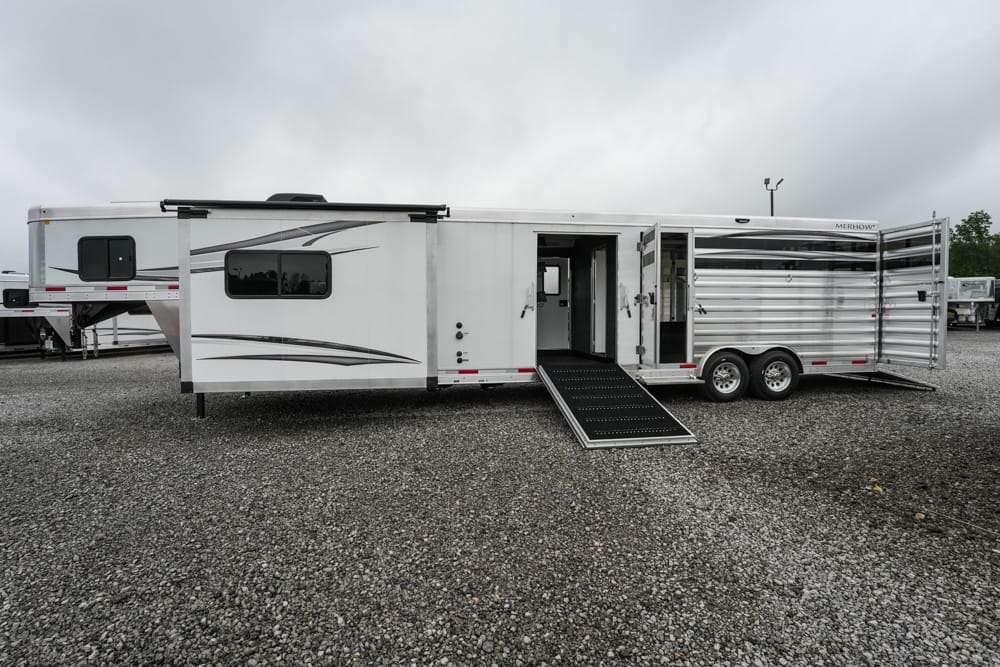 White horse trailer with a lowered loading ramp on a gravel lot, side door open and windows visible.