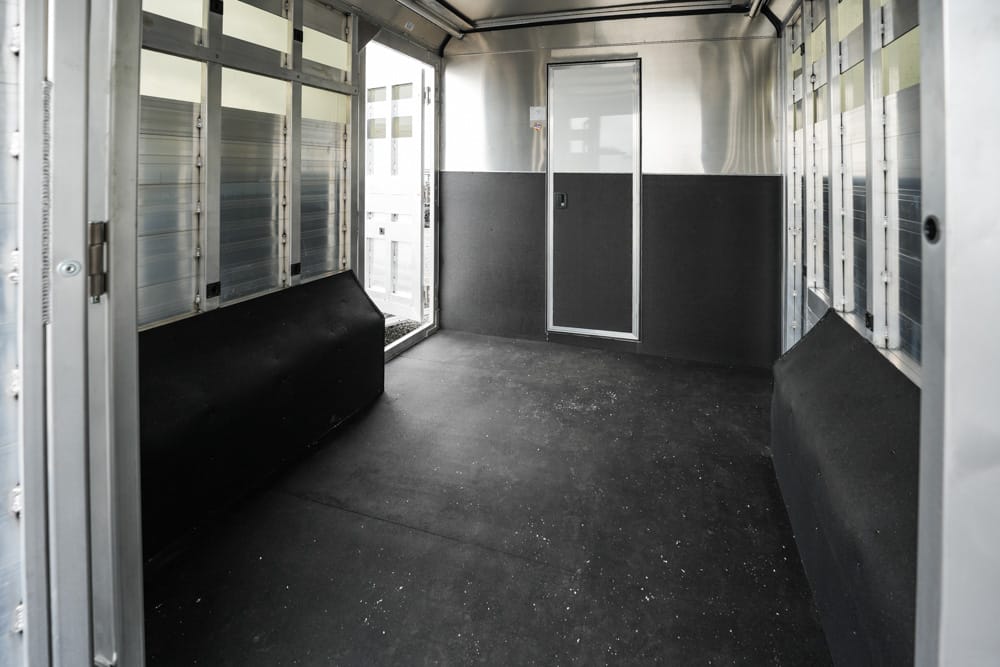 Empty aluminum trailer interior with black padded lower walls and a doorway at the far end.