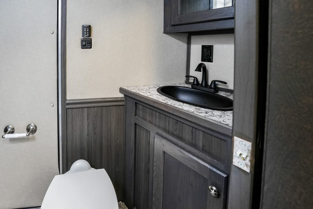 Compact bathroom in an RV with a dark wood vanity, marble countertop, black sink, and a visible toilet in the foreground.