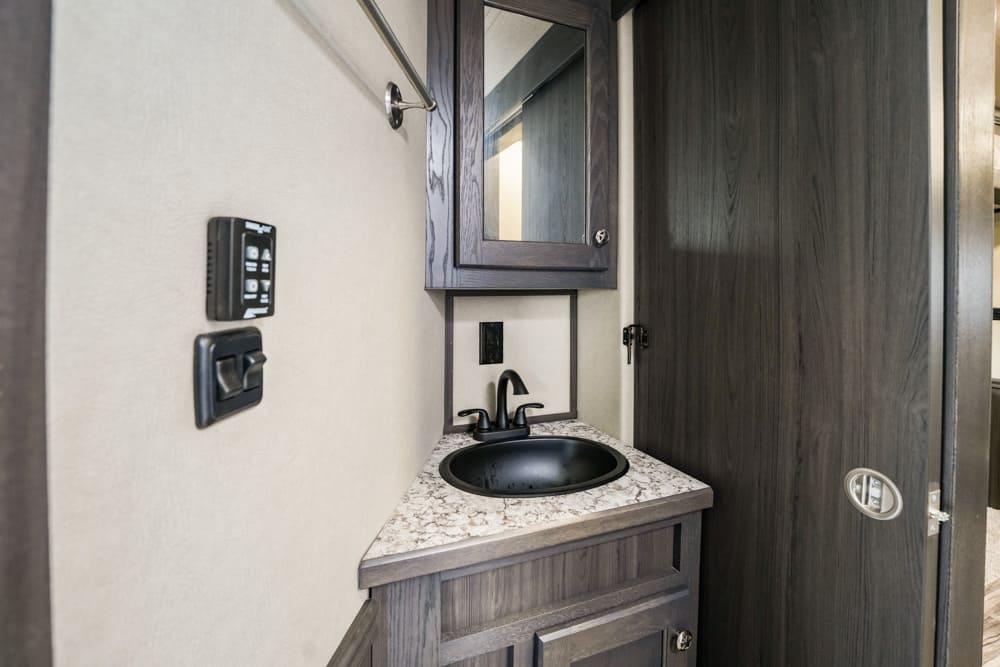 Compact RV bathroom vanity with a black sink, dark wood cabinet, and mirrored medicine cabinet above the counter.