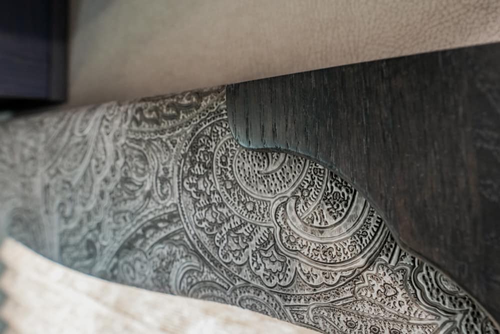 Close-up of a dark wood trim with a curved notch above gray paisley-patterned fabric.