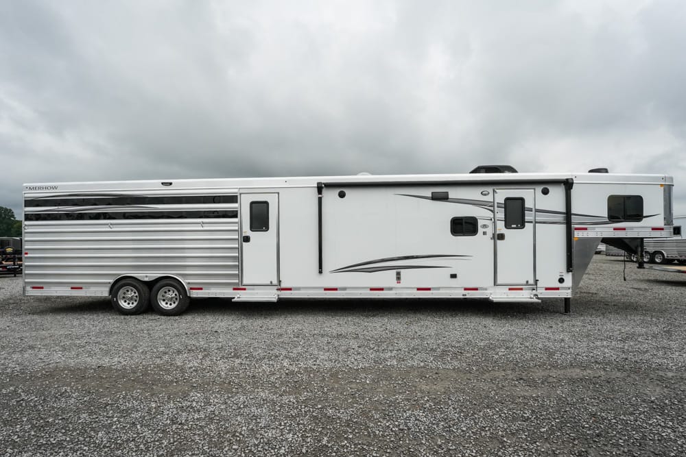 White Merhow horse trailer with two axles parked on a gravel lot under cloudy sky.