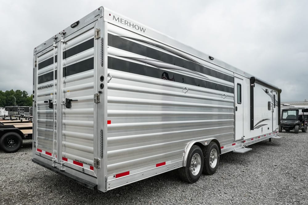 Silver Merhow horse trailer with tandem axles and rear double doors parked on a gravel lot.