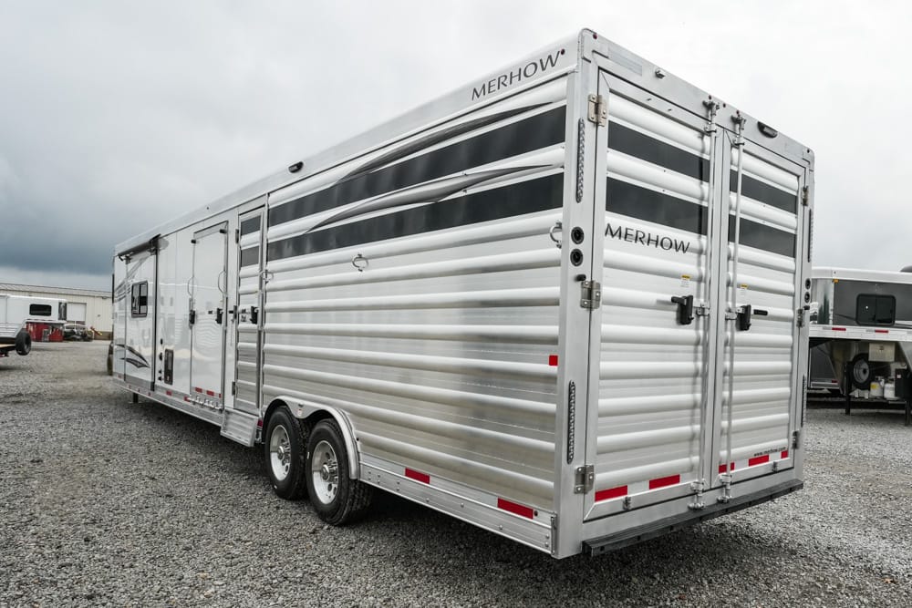 Silver Merhow horse trailer with dual axles parked on a gravel lot, side and rear views visible.
