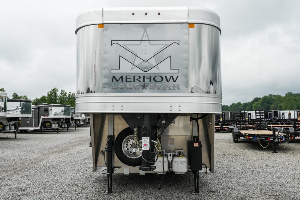 Silver Merhow horse trailer viewed from the back in a gravel lot, with spare tire and equipment beneath and other trailers in the background