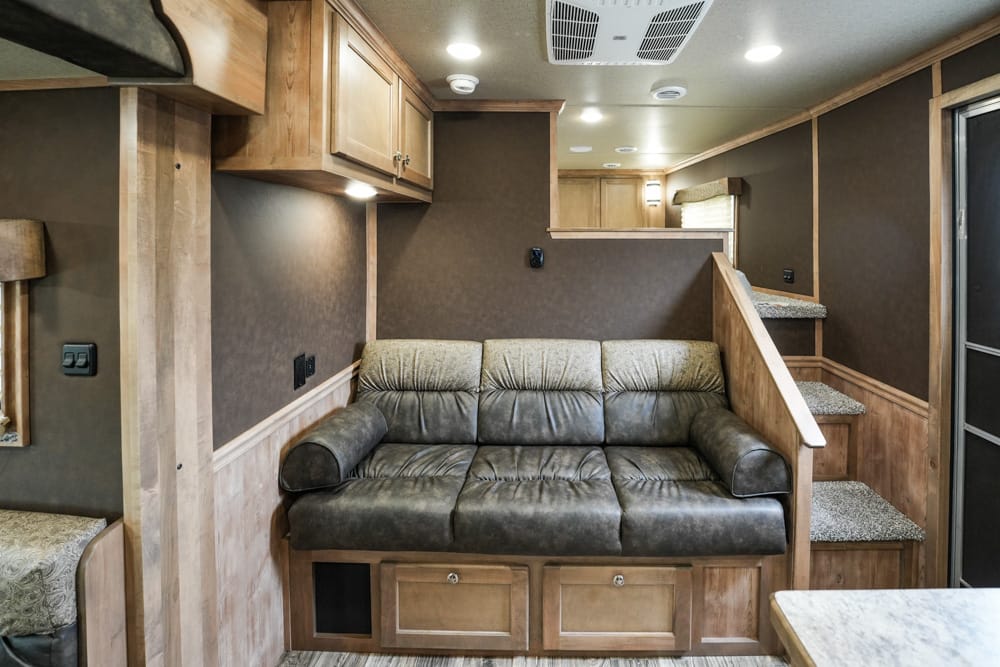 Interior of a motorhome living area featuring a dark leather sofa with storage drawers beneath, wood cabinets above, and a carpeted staircase to the right.