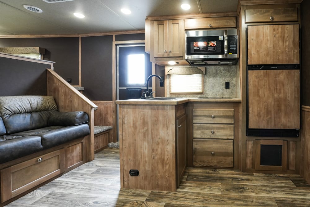 RV kitchen with wooden cabinets, island sink, microwave, and a leather sofa area to the left.