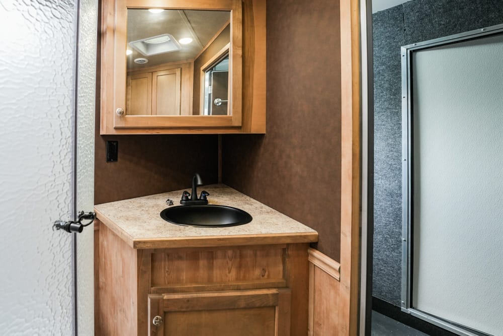 Small bathroom vanity in an RV: beige countertop, black sink, and wood cabinet with a mirrored medicine cabinet above.