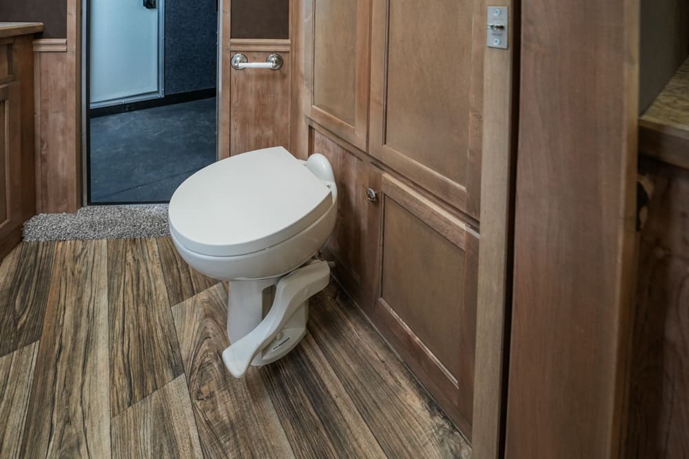 White toilet in a wood-paneled bathroom with wood plank flooring and an open doorway to a hallway.