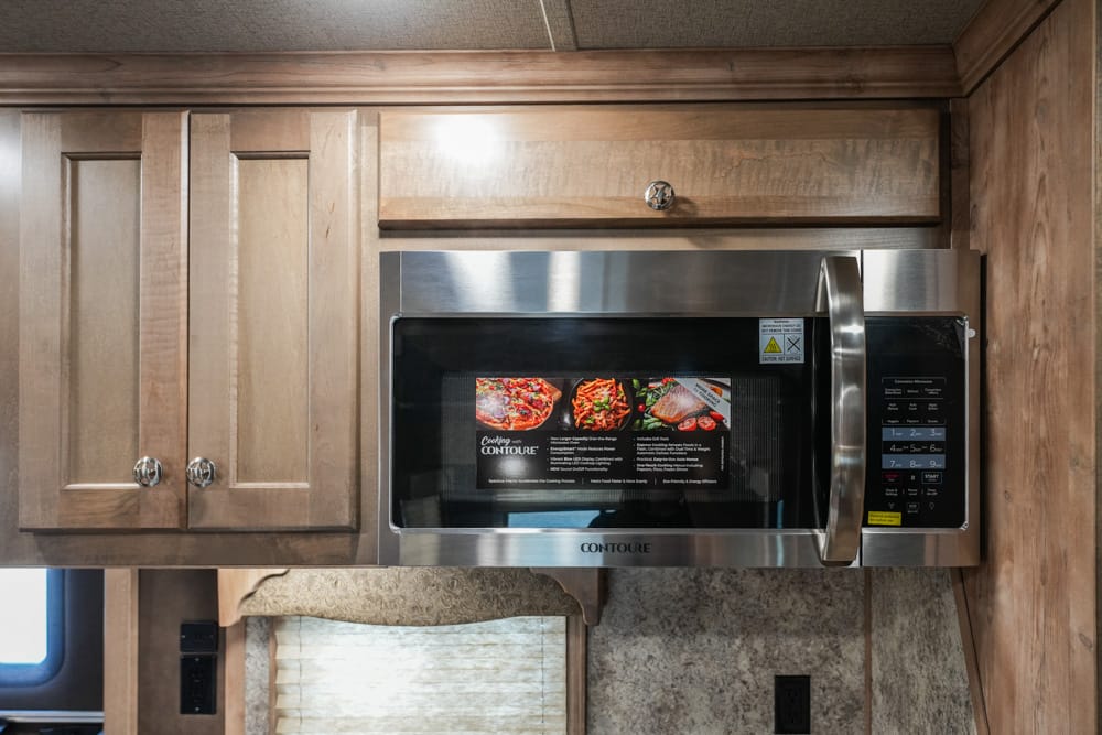 Stainless steel microwave installed in wooden kitchen cabinets, with a control panel on the right and a vent above it