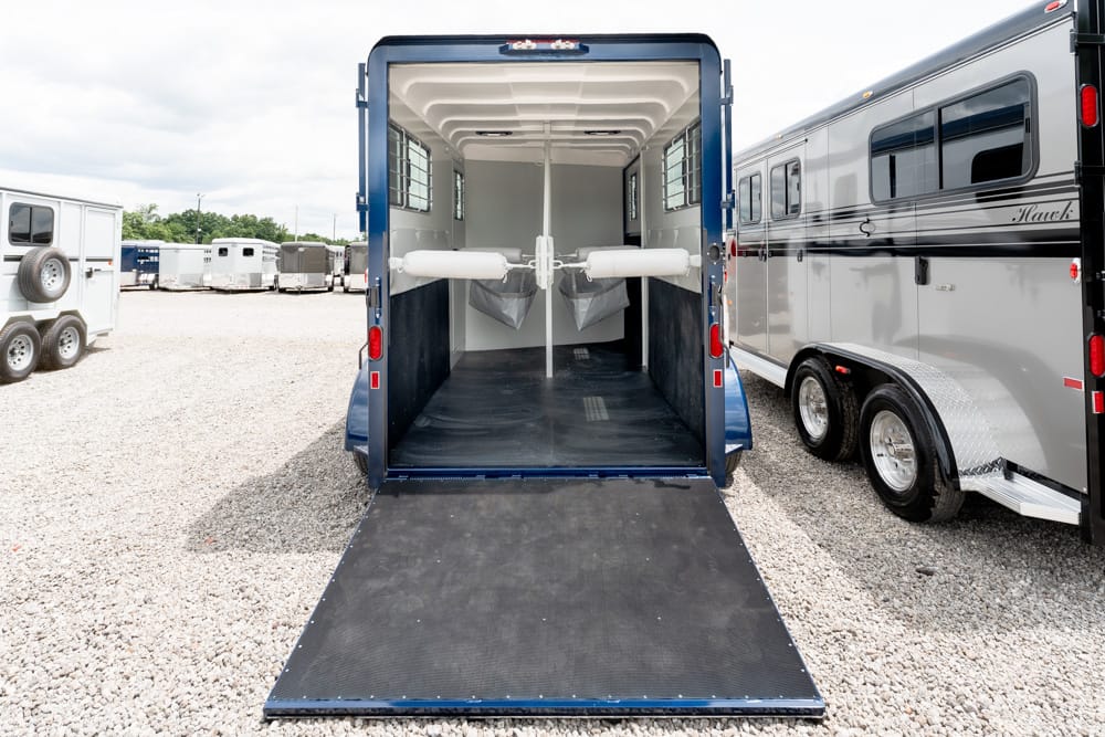 Blue horse trailer with ramp down, interior showing two padded dividers for horses and a black non-slip floor