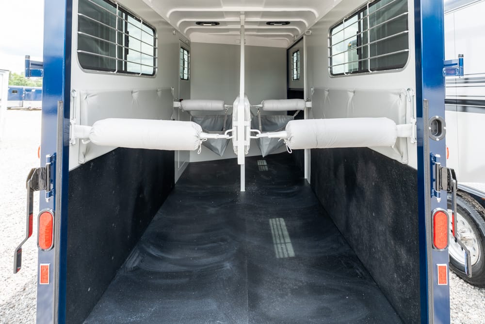 Interior of a horse trailer with four padded stalls and white divider bars, viewed from the open rear doors