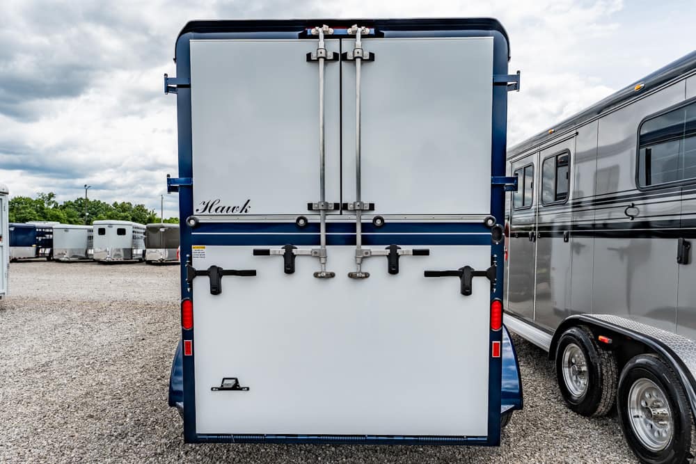 Rear view of a blue-and-white horse trailer with closed double doors and metal latches on a gravel lot
