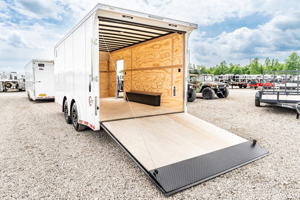 White enclosed cargo trailer with its loading ramp lowered, showing an empty plywood interior ready for loading.