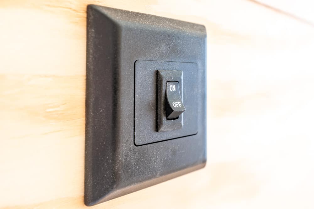 Black wall plate with a small rocker switch labeled ON/OFF, toggled toward ON against a light wood wall