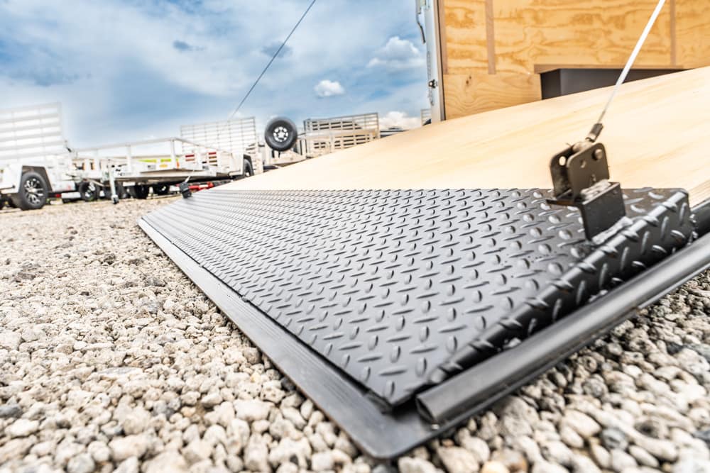Diamond-plate loading ramp on a gravel surface with trailers in the background.