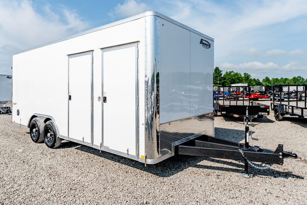 White enclosed cargo trailer with dual rear doors and tandem wheels on a gravel lot.