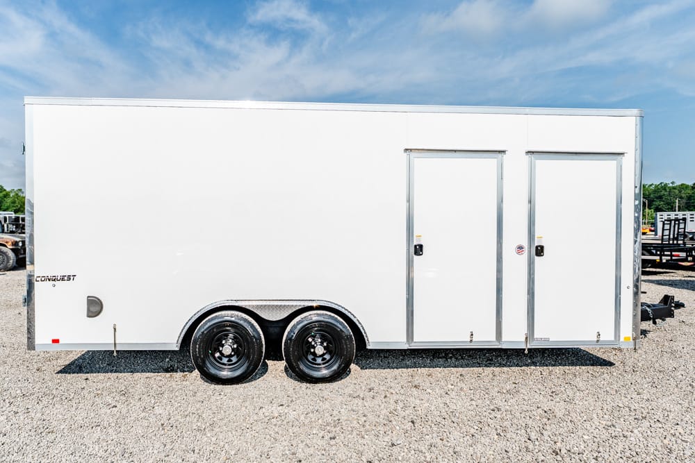 White enclosed cargo trailer with two side doors and dual-axle wheels on a gravel lot.