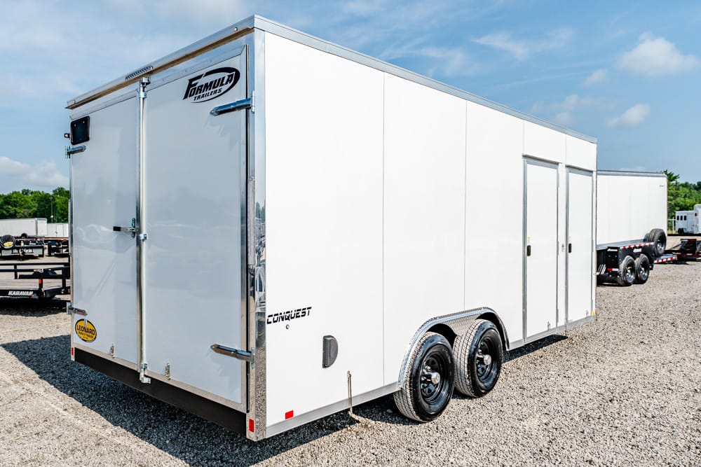 White enclosed, double-axle cargo trailer with rear doors on a gravel lot; side doors visible, brand decals present (Conquest/Formula).