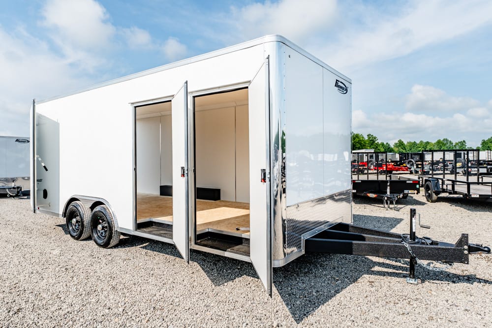White cargo trailer with open side doors showing an empty interior and wooden floor on a gravel lot.