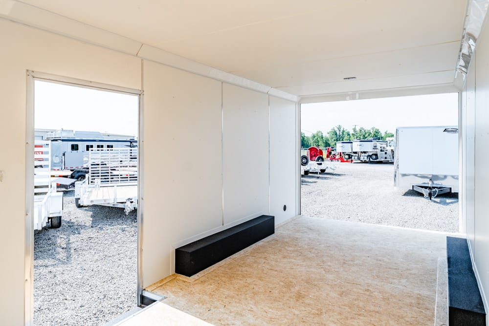 Interior of a white trailer with open doors, revealing a gravel lot with trailers outside