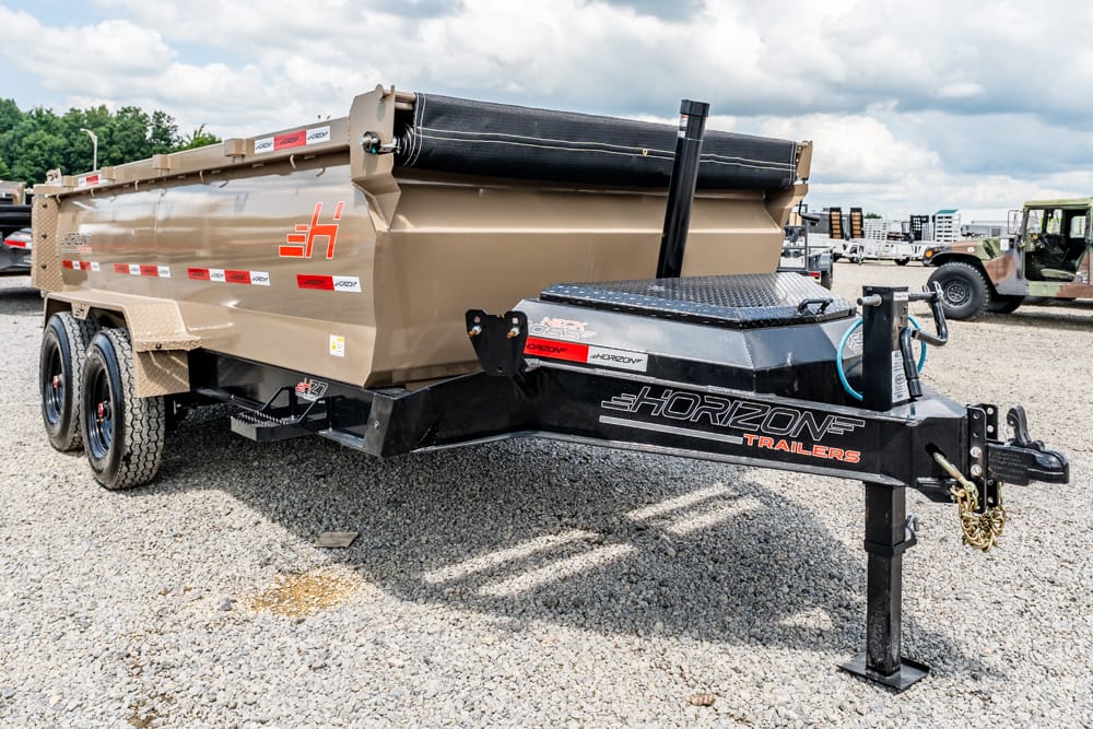 Gooseneck trailer hitch connected to a large tan dump trailer on a gravel lot with a cloudy sky above