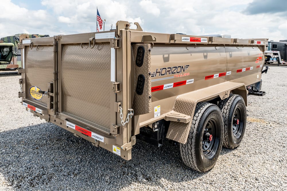Rear and side view of a tan Horizon Trailers dual-axle dump trailer on a gravel lot, with an American flag in the background.