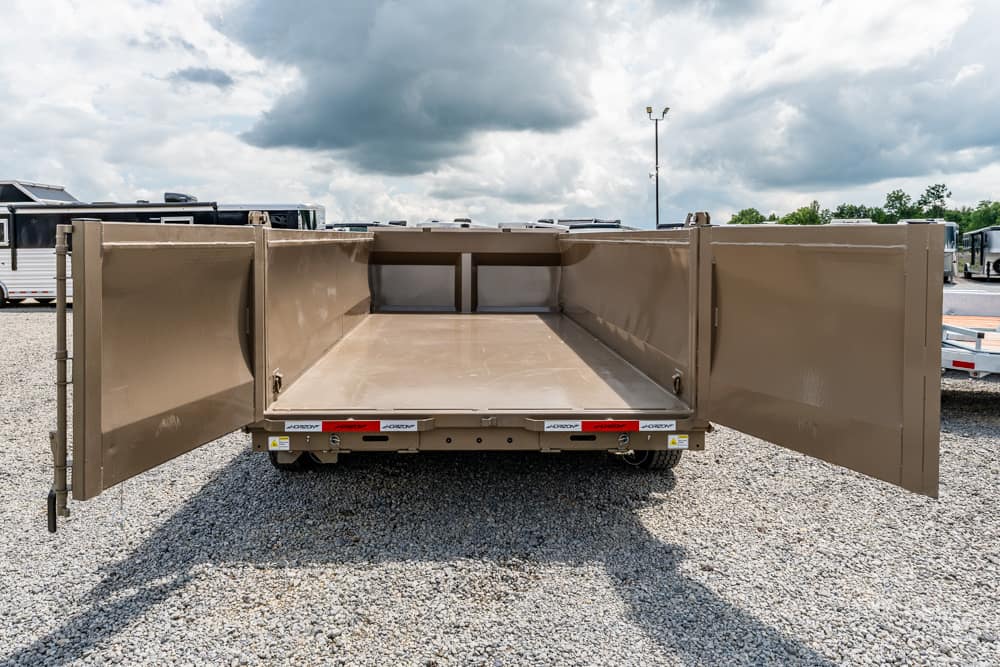 Open beige dump trailer with its rear doors wide open, showing an empty cargo bed on a gravel lot.