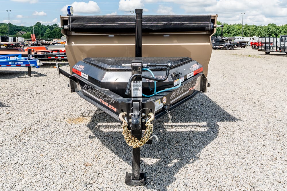 Front view of a Horizon trailer tongue with chains and hitch, a blue hose, and a tan dump trailer in a gravel lot.